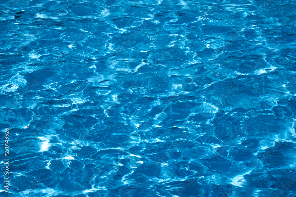 Blue and bright ripple water surface in swimming pool with sun reflection.