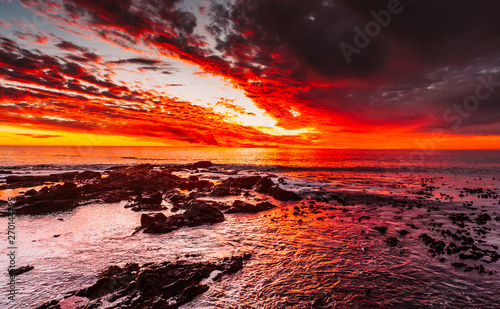 Dramatic nature landscape. Red sunset on the ocean shore. Beautiful sky. Shallow beach of the Pacific ocean