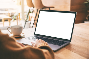 Mockup image of a woman's hand using and touching on laptop touchpad with blank white desktop screen with coffee cup on wooden table
