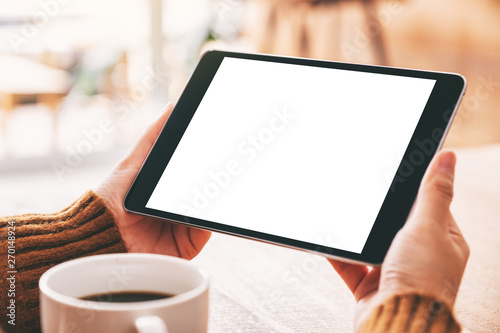 Mockup image of a woman holding black tablet pc with blank white screen with coffee cup on wooden table