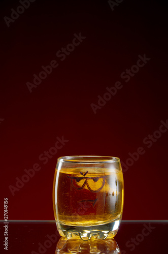 Glass of alcohol with painted eyes dark red background