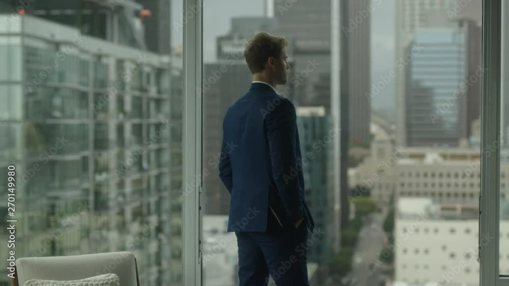 Thoughtful businessman walks around office. Looking on cityscape of downtown and thinking about new projects. Thoughtful businessman walks around office. Looking on cityscape of downtown and thinking about new projects.