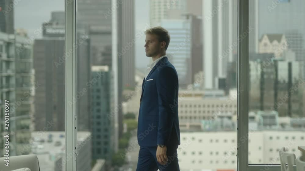 Thoughtful businessman walks around office. Looking on cityscape of downtown and thinking about new projects. 