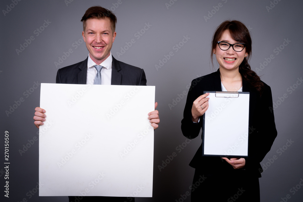 Young businessman and young Asian businesswoman against gray bac Young businessman and young Asian businesswoman against gray bac