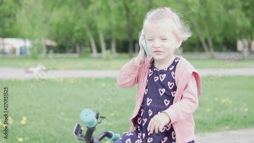 Little girl blonde talking on a toy phone in the park in spring. photo