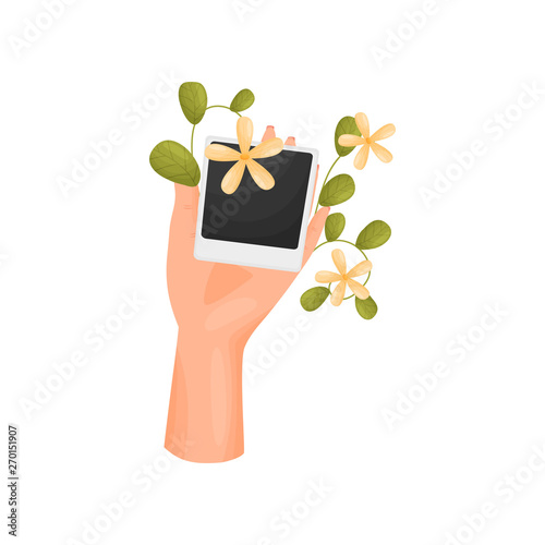 Hand is holding a card with a poloroid and a stem with leaves and flowers. Vector illustration on white background.
