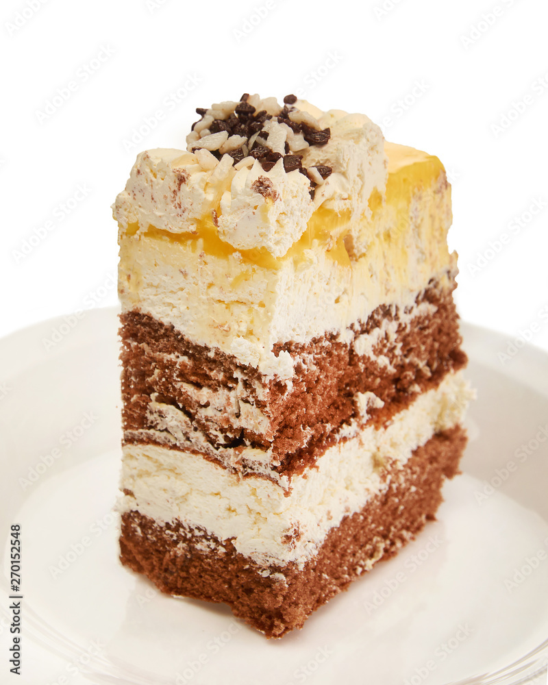 A piece of sweet fresh cake with yellow and chocolate cream on a plate on a white background A piece of sweet fresh cake with yellow and chocolate cream on a plate on a white background
