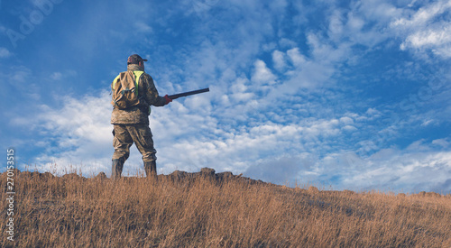 Silhouette of a hunter with a gun in the reeds against the sun, an ambush for ducks with dogs © Mountains Hunter
