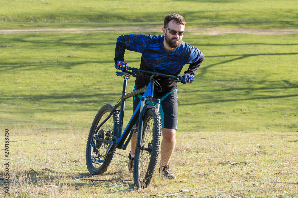 Fototapeta premium Cyclist in shorts and jersey on a modern carbon hardtail bike with an air suspension fork rides off-road on green hills near the forest 