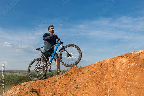 Cyclist in shorts and jersey on a modern carbon hardtail bike with an air suspension fork rides off-road on the orange-red hills at sunset evening in summer