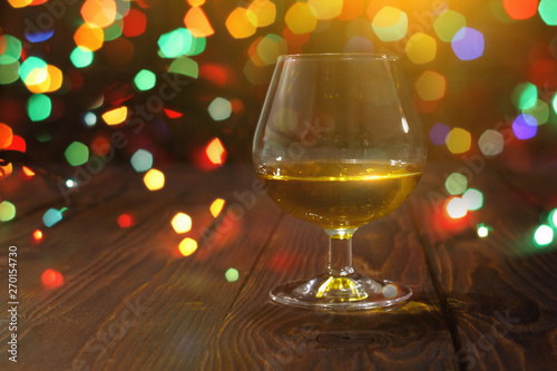 Glass of whiskey or brandy on wooden table on bright glowing background