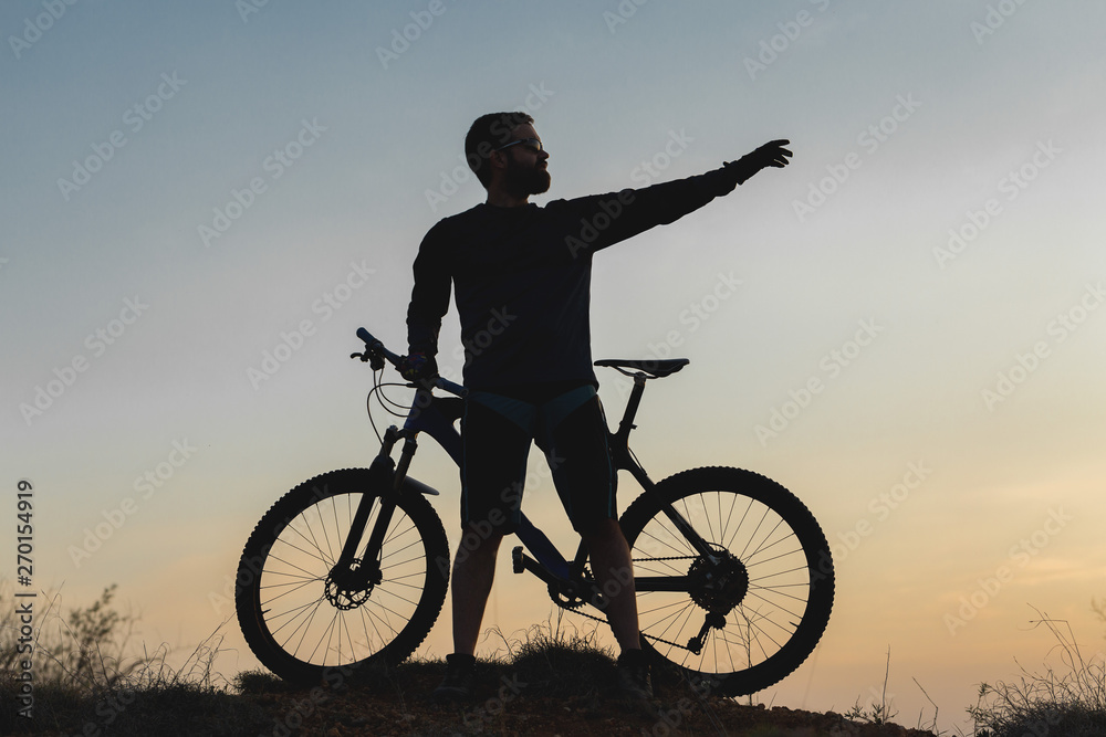 Obraz premium Cyclist in shorts and jersey on a modern carbon hardtail bike with an air suspension fork rides off-road on the orange-red hills at sunset evening in summer