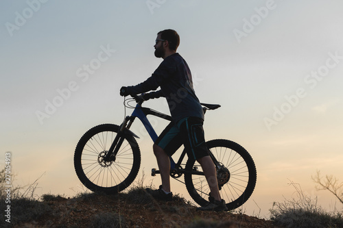 Cyclist in shorts and jersey on a modern carbon hardtail bike with an air suspension fork rides off-road on the orange-red hills at sunset evening in summer