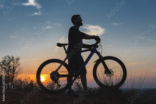 Cyclist in shorts and jersey on a modern carbon hardtail bike with an air suspension fork rides off-road on the orange-red hills at sunset evening in summer