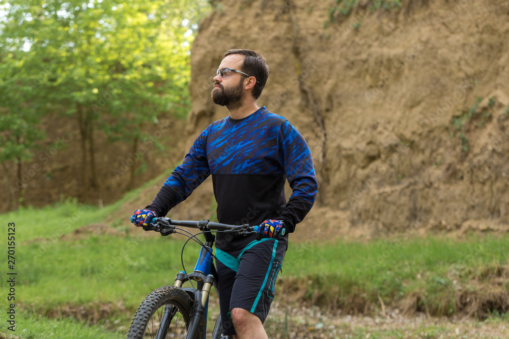 Fototapeta premium Cyclist in shorts and jersey on a modern carbon hardtail bike with an air suspension fork rides off-road on green hills near the forest
