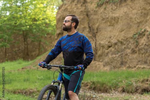 Fototapeta Naklejka Na Ścianę i Meble -  Cyclist in shorts and jersey on a modern carbon hardtail bike with an air suspension fork rides off-road on green hills near the forest	