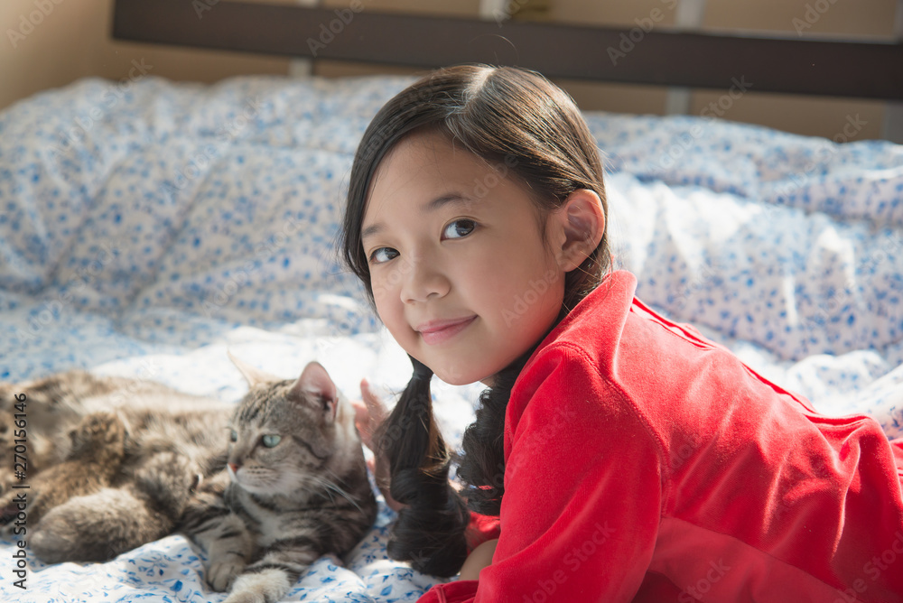 asian girl playing with american short hair cat on the bed