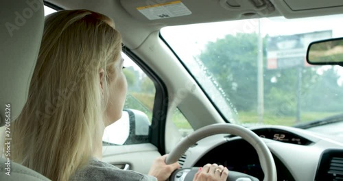 Young blonde caucasian woman driving car with white biright interior during rain  photo
