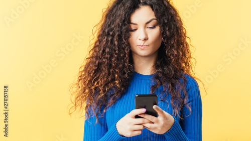 Young woman looking at smartphone. Pursed lips. Skepticism doubt facial expression. Suspicious incredulous wary emotion. photo