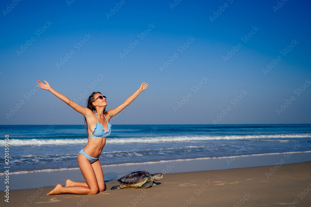 travel girl posing in blue bikini swimsuit looking into the distance and pointing a finger next to a big male turtle lifestyle vacation paradise untouched deserted beach morning.tourism guide concept travel girl posing in blue bikini swimsuit looking into the distance and pointing a finger next to a big male turtle lifestyle vacation paradise untouched deserted beach morning.tourism guide concept