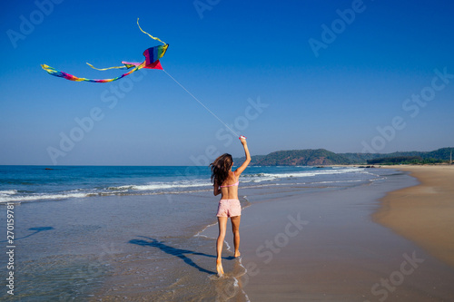 happy brunette girl in a bathing suit and short pink playing with flying kite on tropical beach copyspase