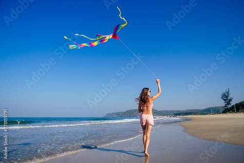 happy brunette girl in a bathing suit and short pink playing with flying kite on tropical beach copyspase