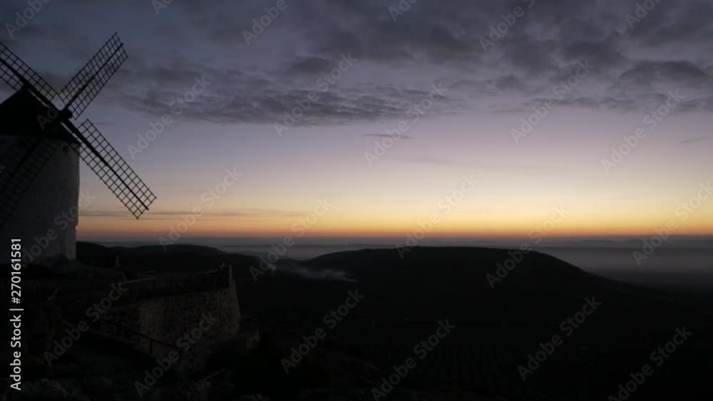 A panning towards right starting on a windmill from top of a mountain in the middle of a plain, with mist near the ground at foreground. Shoted before the sunshine, in Castilla la Mancha, Spain.