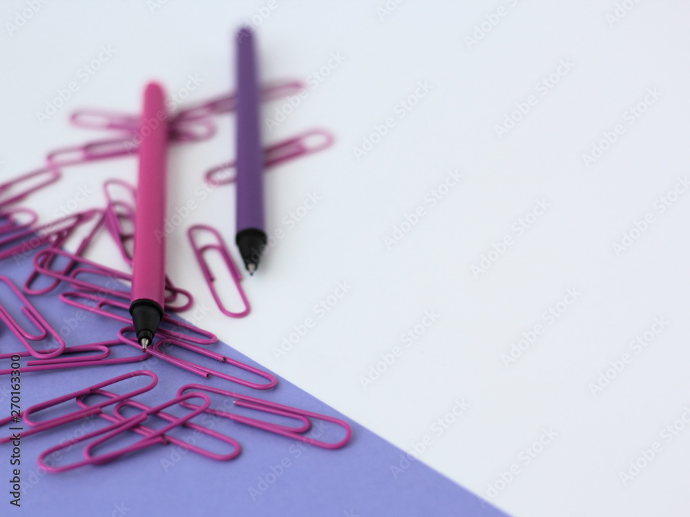 Fototapeta premium Closeup of purple stationery. Pens and paperclips on white and purple backgrund.