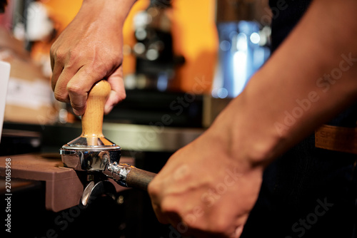 Close-up of barmen working in bar and grinding coffee beans to prepare fresh black coffee drink