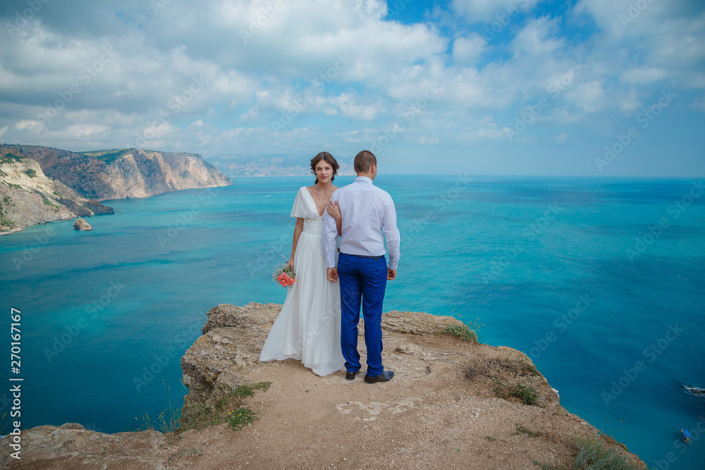 Beautiful couple on the sea rocks in wedding dress. Just married view from behind.