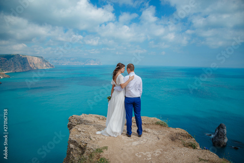 Beautiful couple on the sea rocks in wedding dress. Just married view from behind.