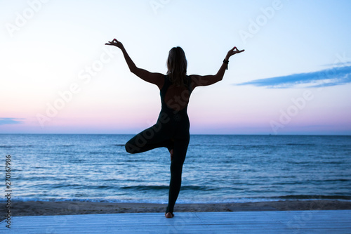 woman doing yoga at sunrise on the sea, silhouette of yoga poses © AlexR