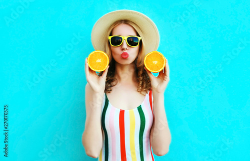 Summer portrait woman holding in her hands two slices of orange fruit in straw hat on colorful blue background