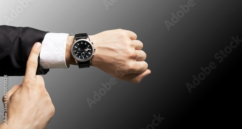Businessman pointing at hand watch on grey wall background, close-up