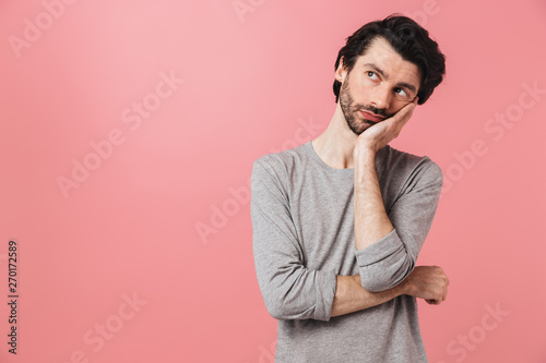 Handsome thinking young man isolated over pink wall background.
