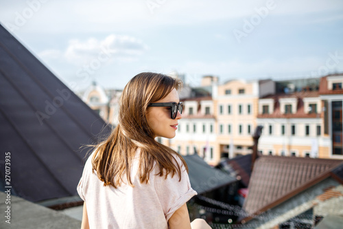 A young European brunette woman sits on the roof and enjoys a beautiful view of the height. Enjoy your time. Close-up.
