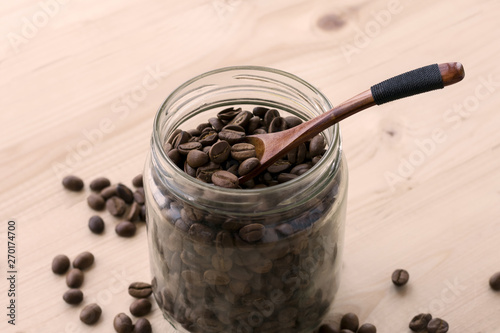 Roasted coffee beans in a glass jar with wooden spoon