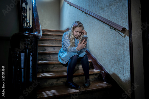Sad depressed unhappy child suffering from cyberbullying by mobile smart phone sitting alone.