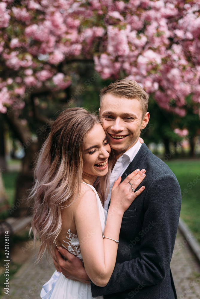Naklejka premium cute couple standing under a flowering tree hugging and smiling
