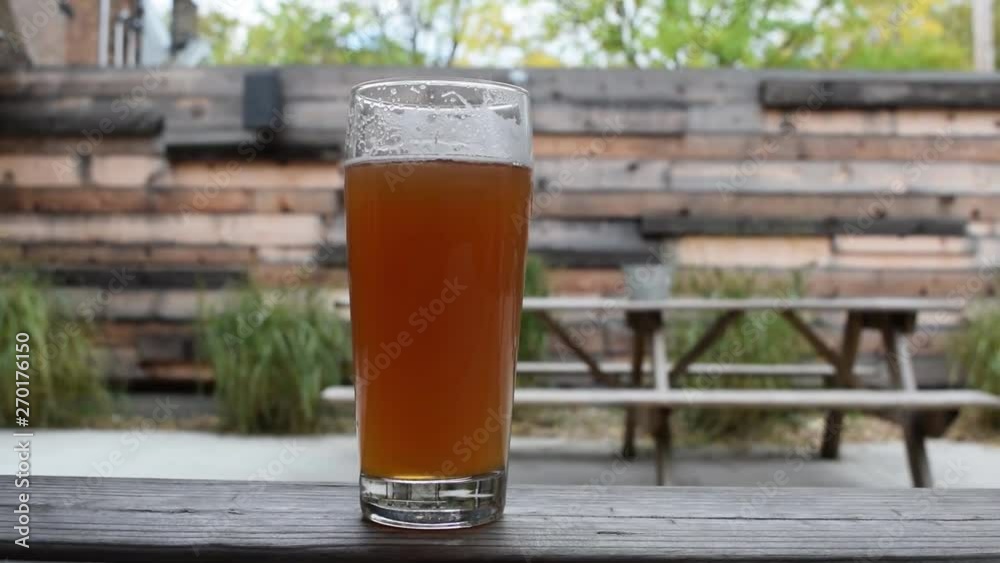 A tall glass of fresh beer on a picnic table in a backyard on a nice summer sunny day. A tall glass of fresh beer on a picnic table in a backyard on a nice summer sunny day.