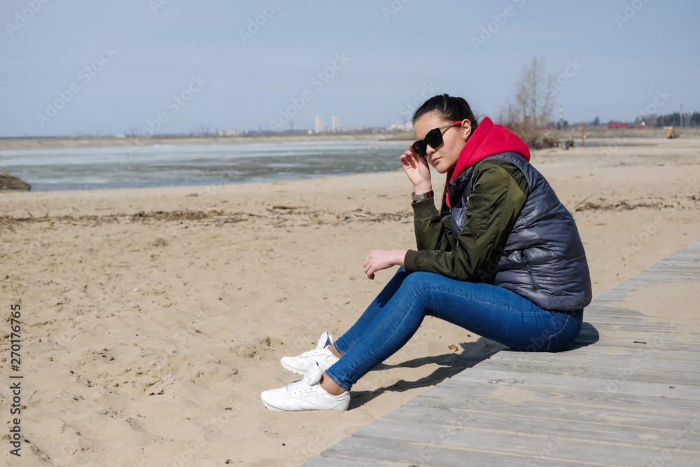Young woman on the beach in warm clothes. A girl in a red hoodie wears a hood over her head.