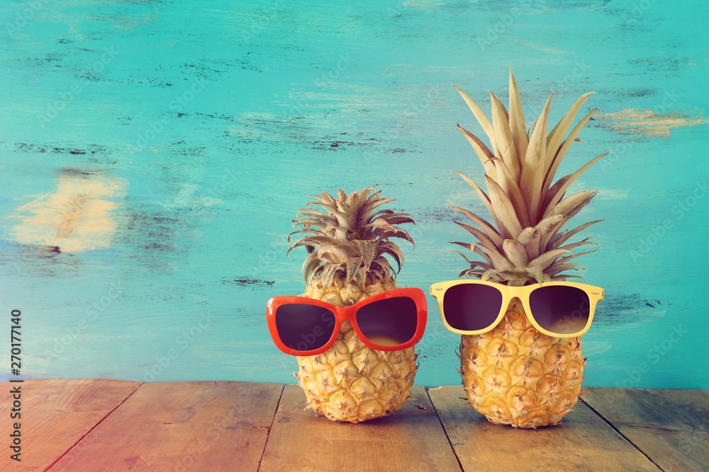 Ripe couple pineapple in stylish sunglasses over wooden table or deck, relaxing. Tropical summer vacation concept