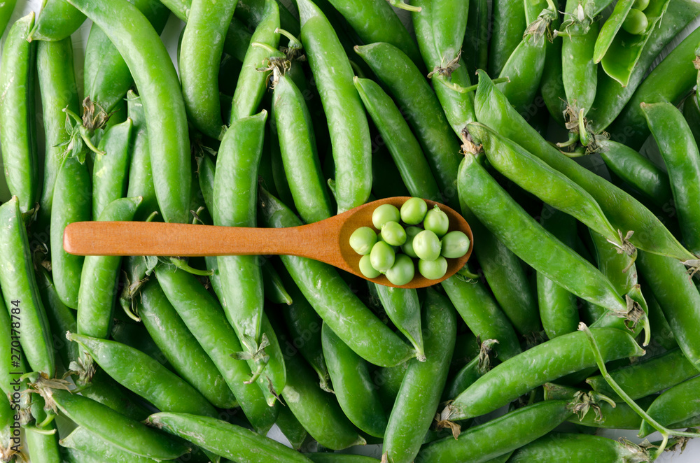 Fototapeta premium Top view of spoon of peas.Peas in pods as a background