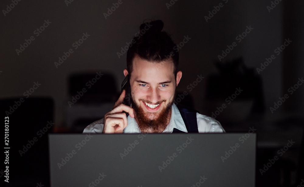A portrait of young businessman with smartphone in an office at night, working. A portrait of young businessman with smartphone in an office at night, working.