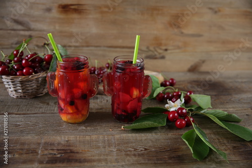 Berries and citrus infused water cocktail, compote, lemonade or tea. Summer iced cold drink with berries, cherry, lemon on a wooden rustic background with branch of cherry . With copy space for text.