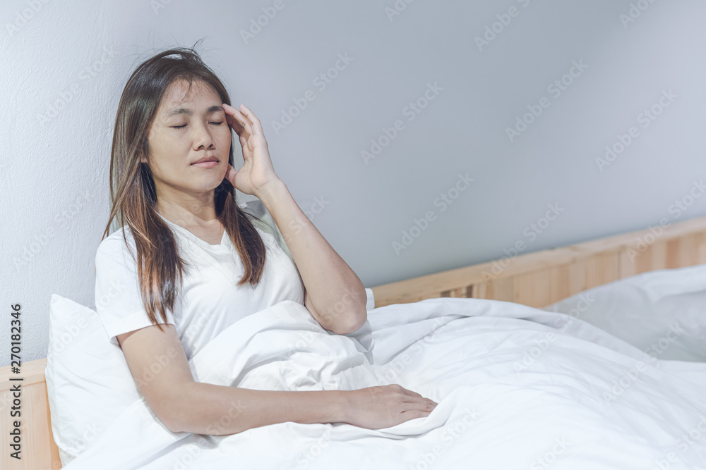 Young asian woman feeling headache and discomfort on white bed in her bedroom.