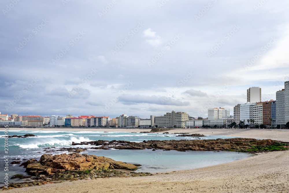 View of the city of Coruña in Galicia Spain from the Riazor Beach with rocks on the shore with a cloudy sky	