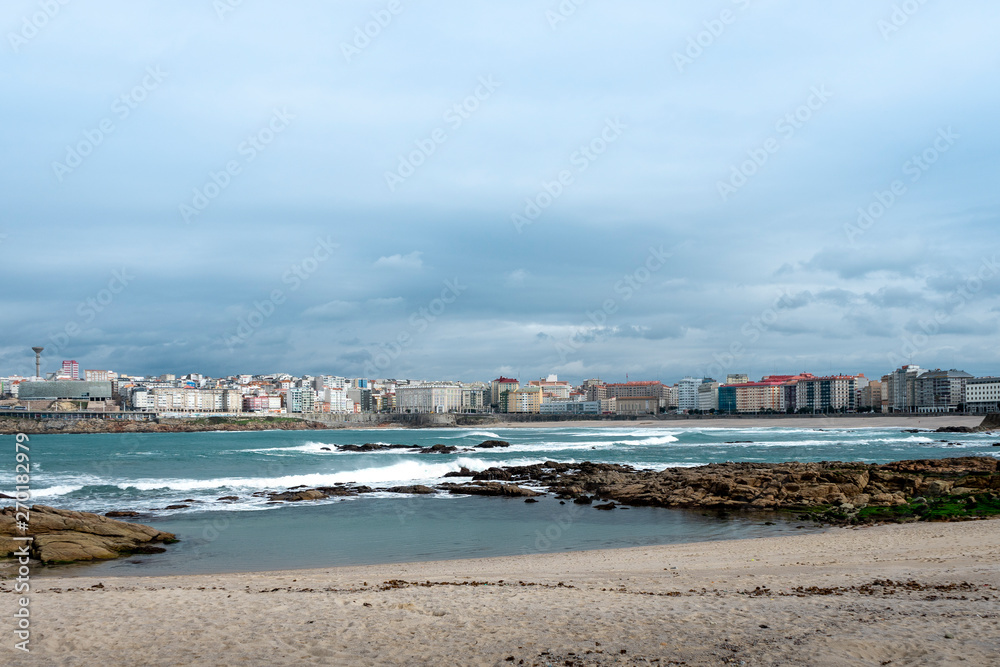 View of the city of Coruña in Galicia Spain from the Riazor Beach with rocks on the shore with a cloudy sky 