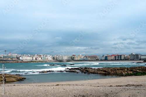 View of the city of Coruña in Galicia Spain from the Riazor Beach with rocks on the shore with a cloudy sky 