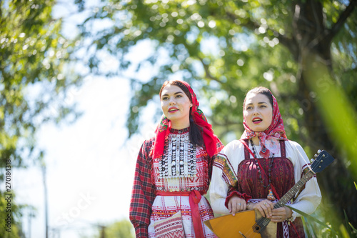 Two young women in traditional russian clothes walk holding hands and singing